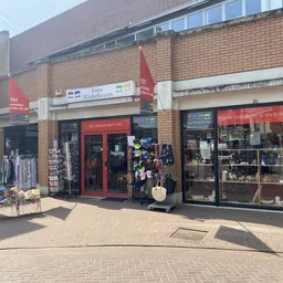 Gevel van kringloopwinkel met rode deuren, etalages en rode vlaggen, aan het Koopmansplein