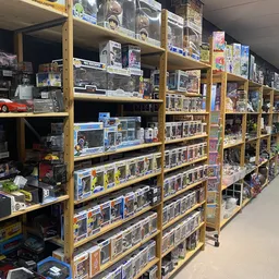 Gele stellingen volgestapeld met verzamelfiguren, speelgoed en collectibles in dozen en verpakkingen
