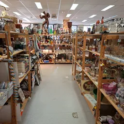 Binnenaanzicht van kringloopwinkel met houten stellingen vol spullen aan weerszijden van middenpad