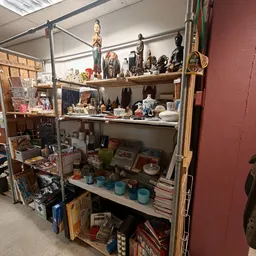 Stellingkast met diverse tweedehands spullen: beelden, flessen, servies, boeken en huishoudartikelen