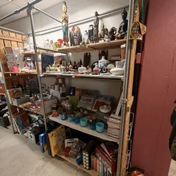 Stellingen met diverse huishoudelijke artikelen, servies, flessen en decoratieve voorwerpen in een kringloopwinkel