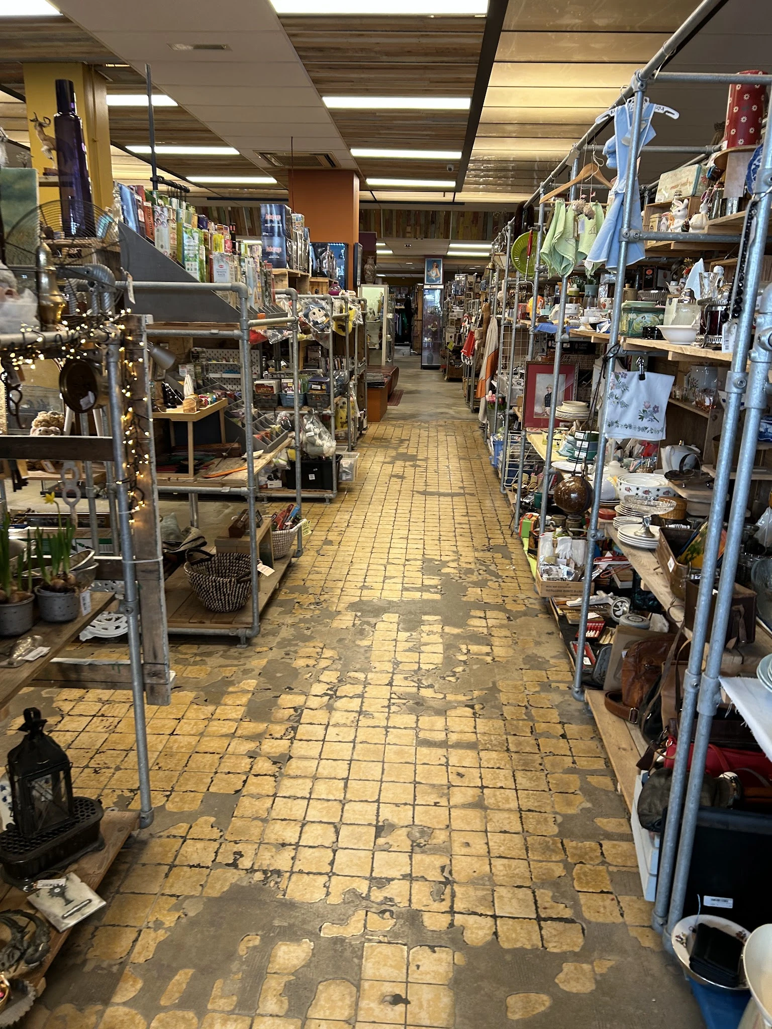 Zicht op de winkelvloer van een kringloopwinkel met stellingen aan beide zijden vol spullen