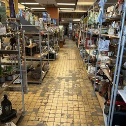 Zicht op de winkelvloer van een kringloopwinkel met stellingen aan beide zijden vol spullen