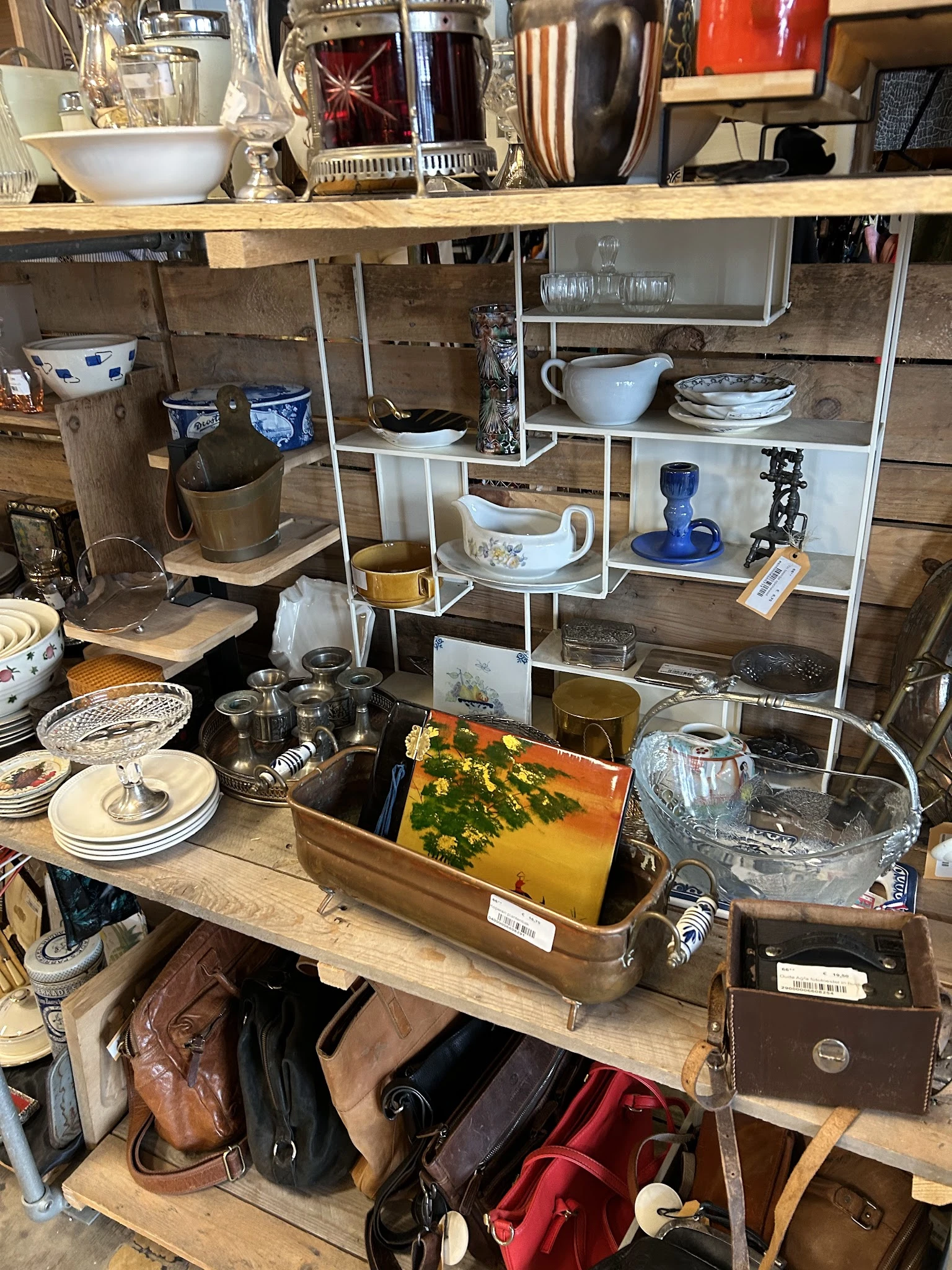 Uitgestalde tweedehands huishoudartikelen: serviesgoed, kopjes, kannen en decoratieve items op tafel en stellingen