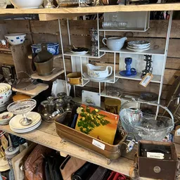 Uitgestalde tweedehands huishoudartikelen: serviesgoed, kopjes, kannen en decoratieve items op tafel en stellingen