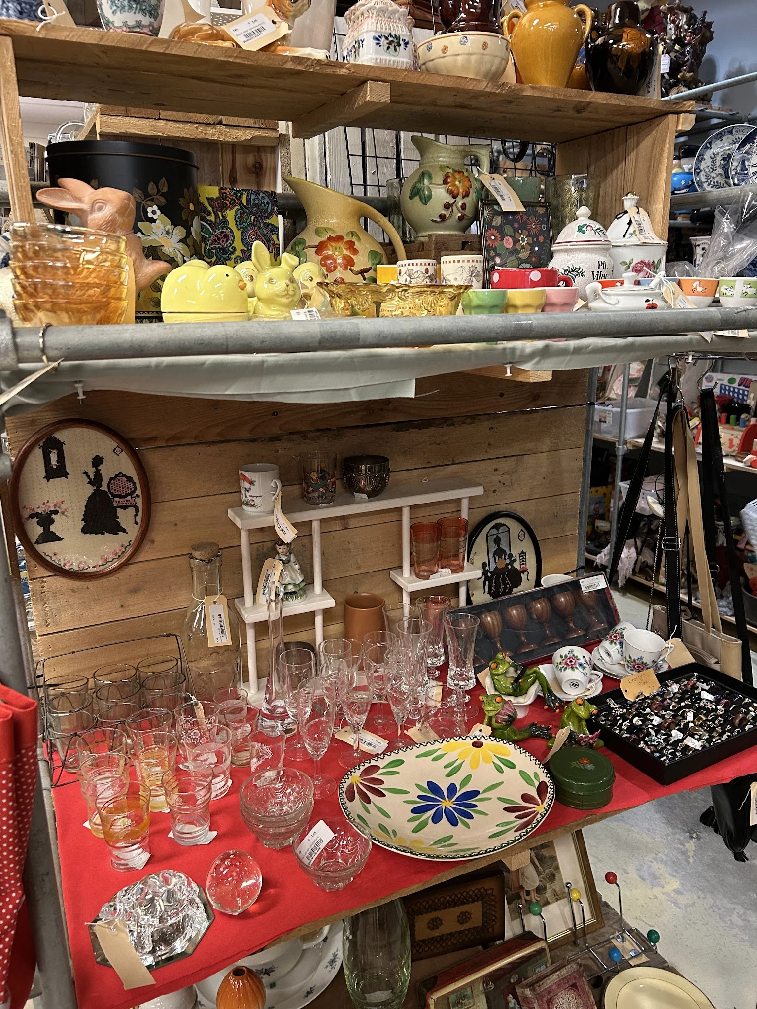 Uitgestalde huishoudartikelen en serviesgoed in een kringloopwinkel, waaronder glazen, bordjes en decoratieve voorwerpen