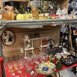Uitgestalde huishoudartikelen en serviesgoed in een kringloopwinkel, waaronder glazen, bordjes en decoratieve voorwerpen