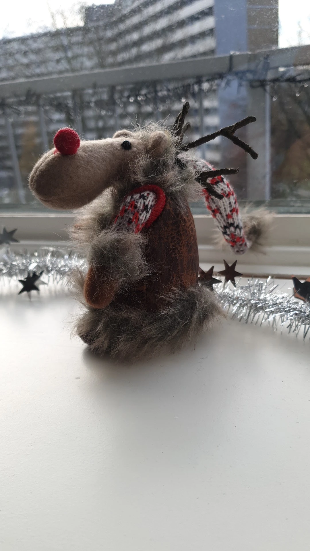 Handgebreide grijze muis met rode wanten en zilveren kerstversiering op een vensterbank