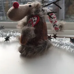 Handgebreide grijze muis met rode wanten en zilveren kerstversiering op een vensterbank