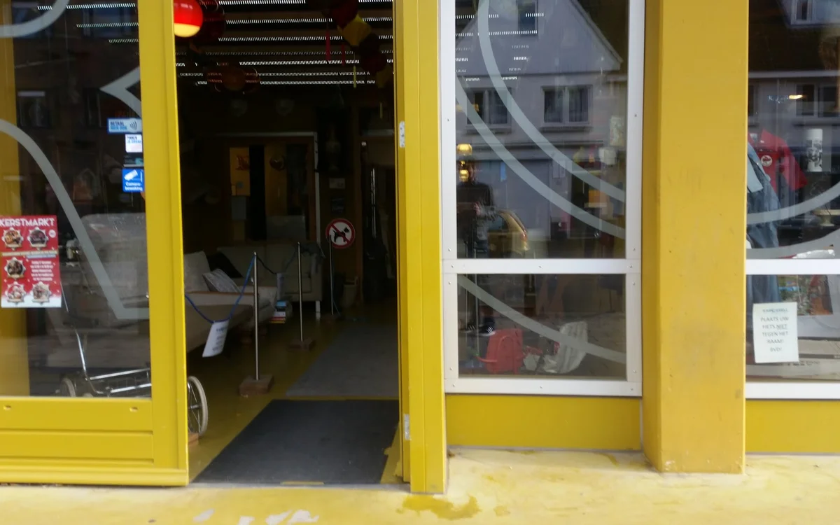 Gele winkelfront met open deuren en grote ramen, zicht op winkelinterieur met stellingen