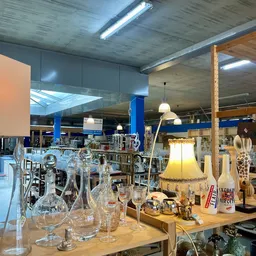 Uitgestalde huishoudelijke artikelen en decoratie in de kringloopwinkel, waaronder glazen, lampen en keramiek op houten tafel