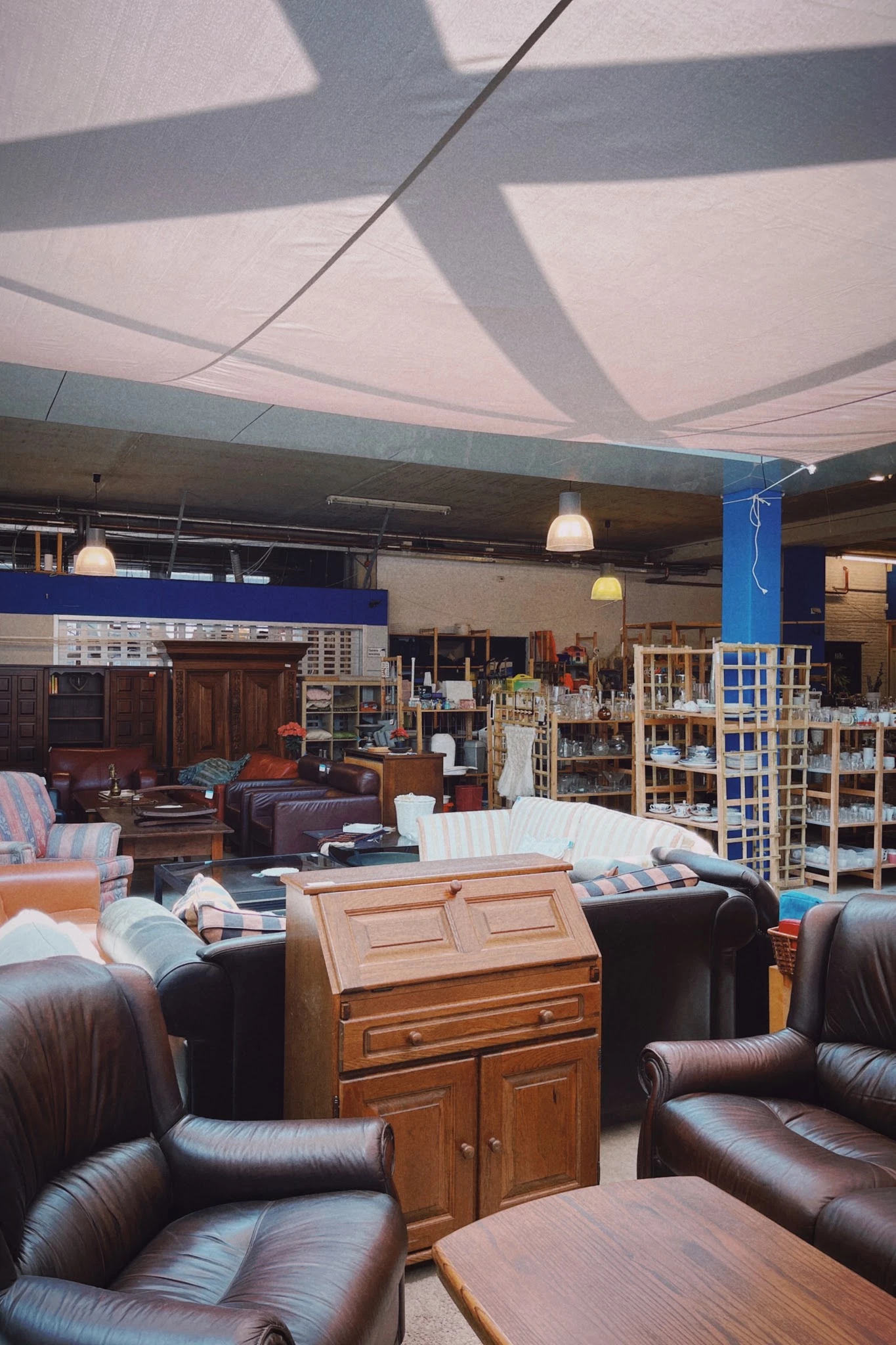 Ruim winkelinterieur met meubels, stellingen met spullen, hangende lampen en betonnen plafond