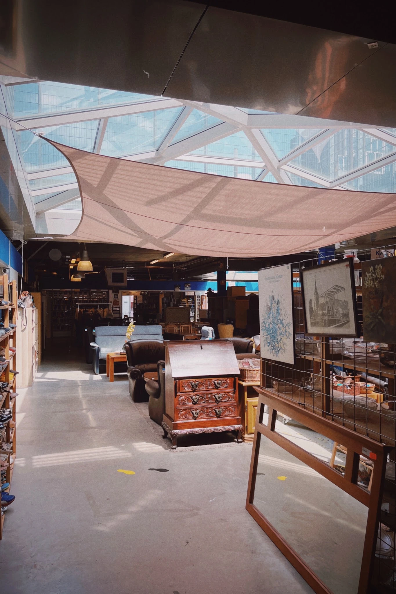 Overzicht van kringloopwinkel met diverse meubels, kasten en spullen onder afdakking met zonnescherm