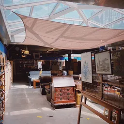 Overzicht van kringloopwinkel met diverse meubels, kasten en spullen onder afdakking met zonnescherm