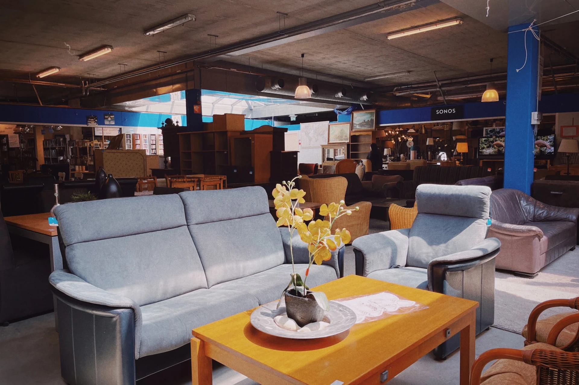 Zithoek met grijze en roze stoelen, gele tafel en gele bloemen in kringloopwinkel