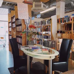 Binnenaanzicht kringloopwinkel met boekenrekken, leeshoek met tafel en stoelen, en plantenversiering