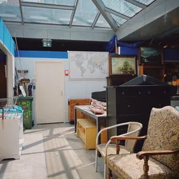 Winkelvloer met meubels, stoelen, een zwarte kast en uitgestalde spullen in een kringloopwinkel