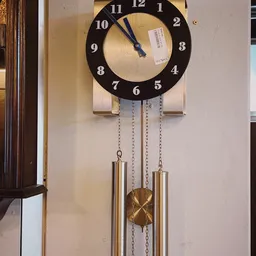 Zwarte wandklok met hoefijzervorm en hangende messingbuizen, close-up van klokwerk