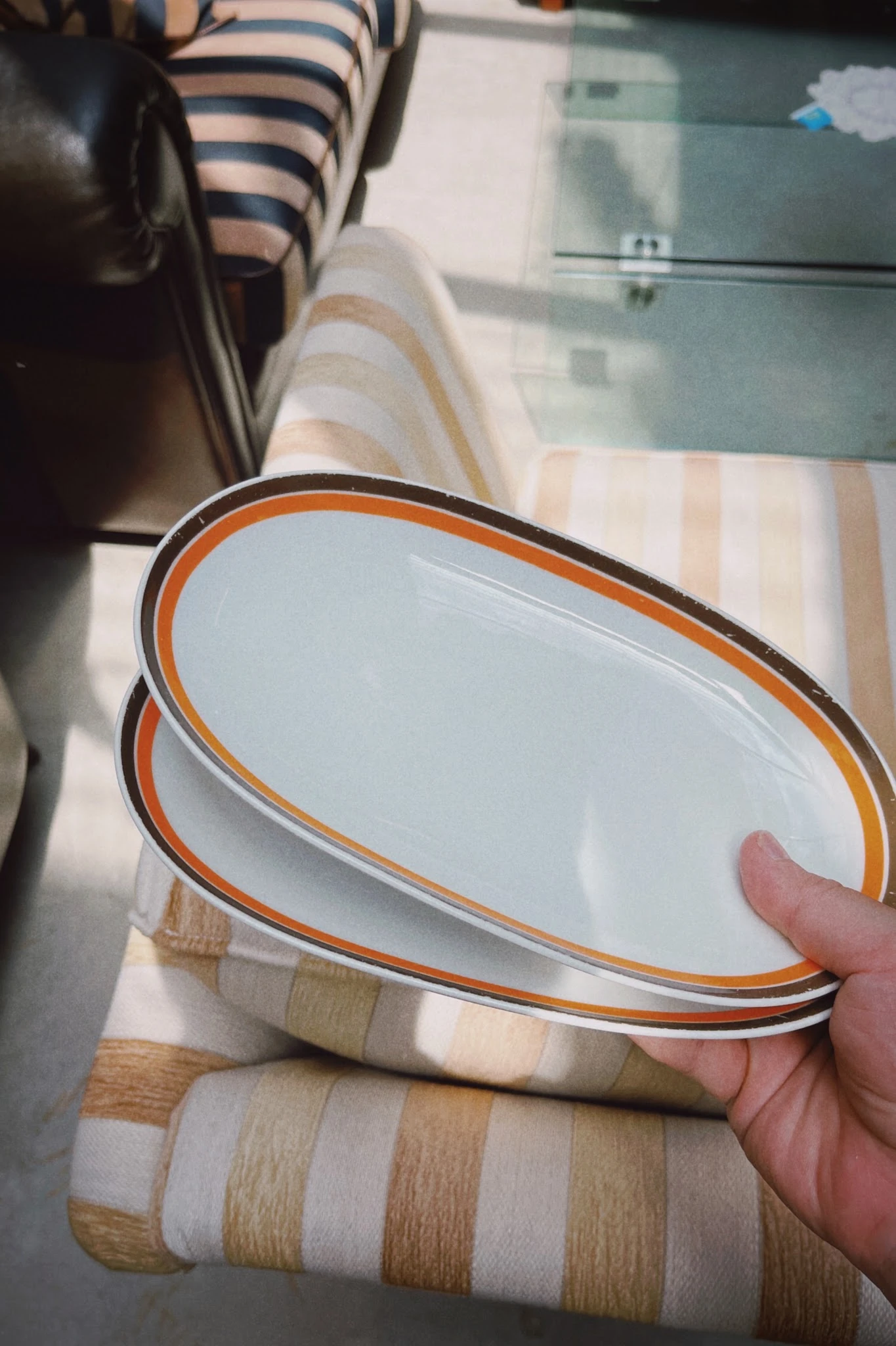 Close-up van een wit emaille servies met oranje rand, gehouden in een hand