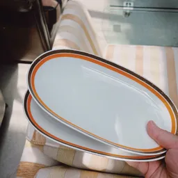 Close-up van een wit emaille servies met oranje rand, gehouden in een hand