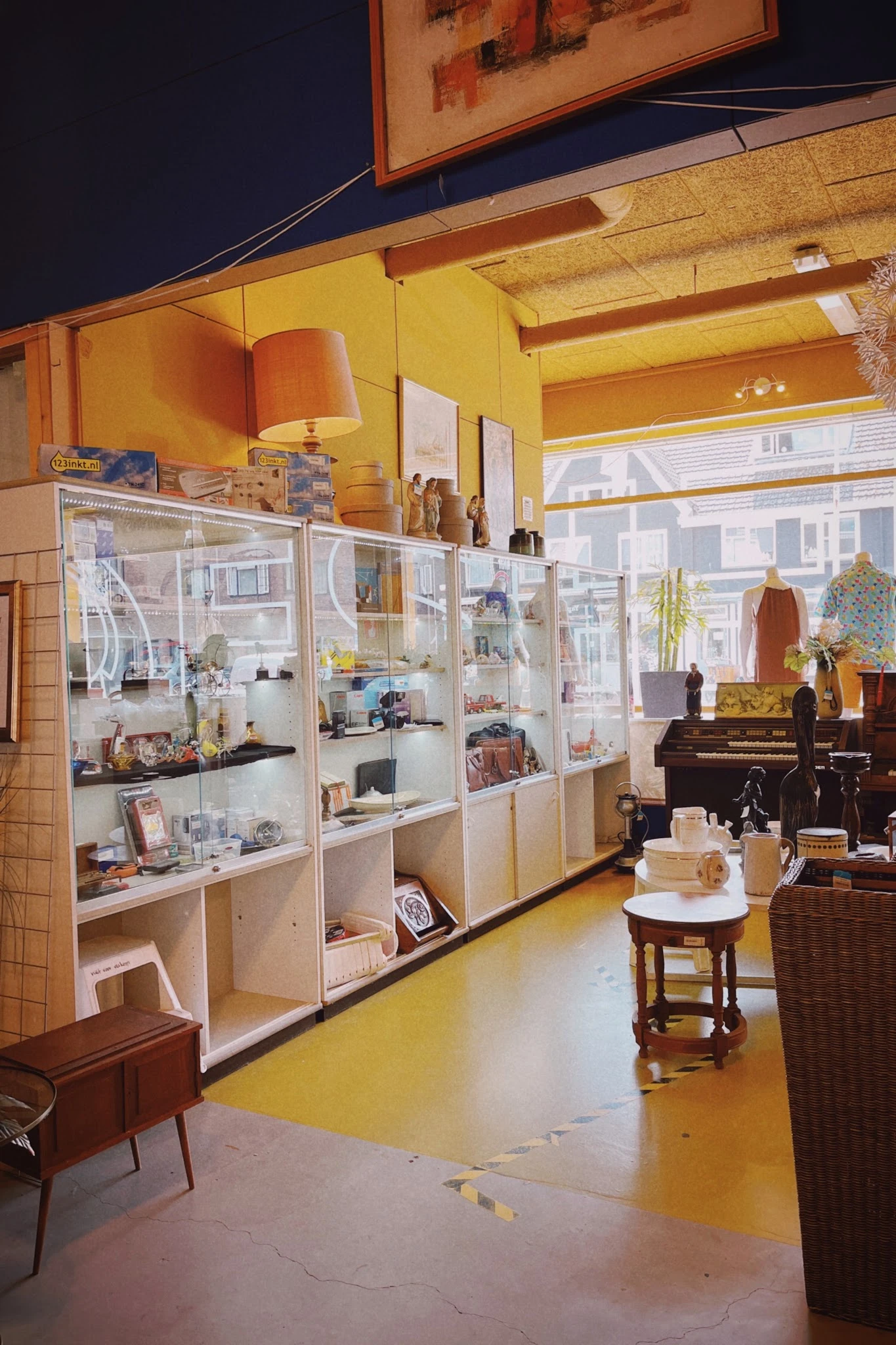 Winkelinterieur met glazen vitrinekasten vol decoratiespullen en antiekartikelen, piano op de achtergrond