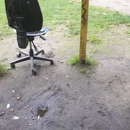 Kantoorstoel op wieltjes buiten op een modderig terras naast een houten paal