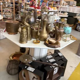 Uitgestalde gouden en messingkleurige decoratieobjecten, vazen en beeldjes op een witte tafel in de winkel