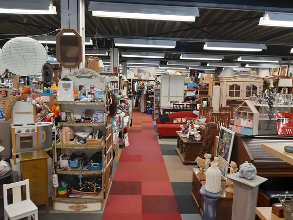 Winkelvloer van kringloopwinkel met stellingen, meubels en huishoudartikelen langs rode en grijze tegelvloer