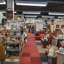 Winkelvloer van kringloopwinkel met stellingen, meubels en huishoudartikelen langs rode en grijze tegelvloer