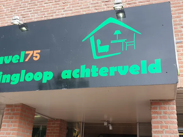 Grijze gevel met groen neonbord van kringloopwinkel met huisicon en tekst 'ingloop achterveld'