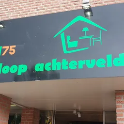 Grijze gevel met groen neonbord van kringloopwinkel met huisicon en tekst 'ingloop achterveld'