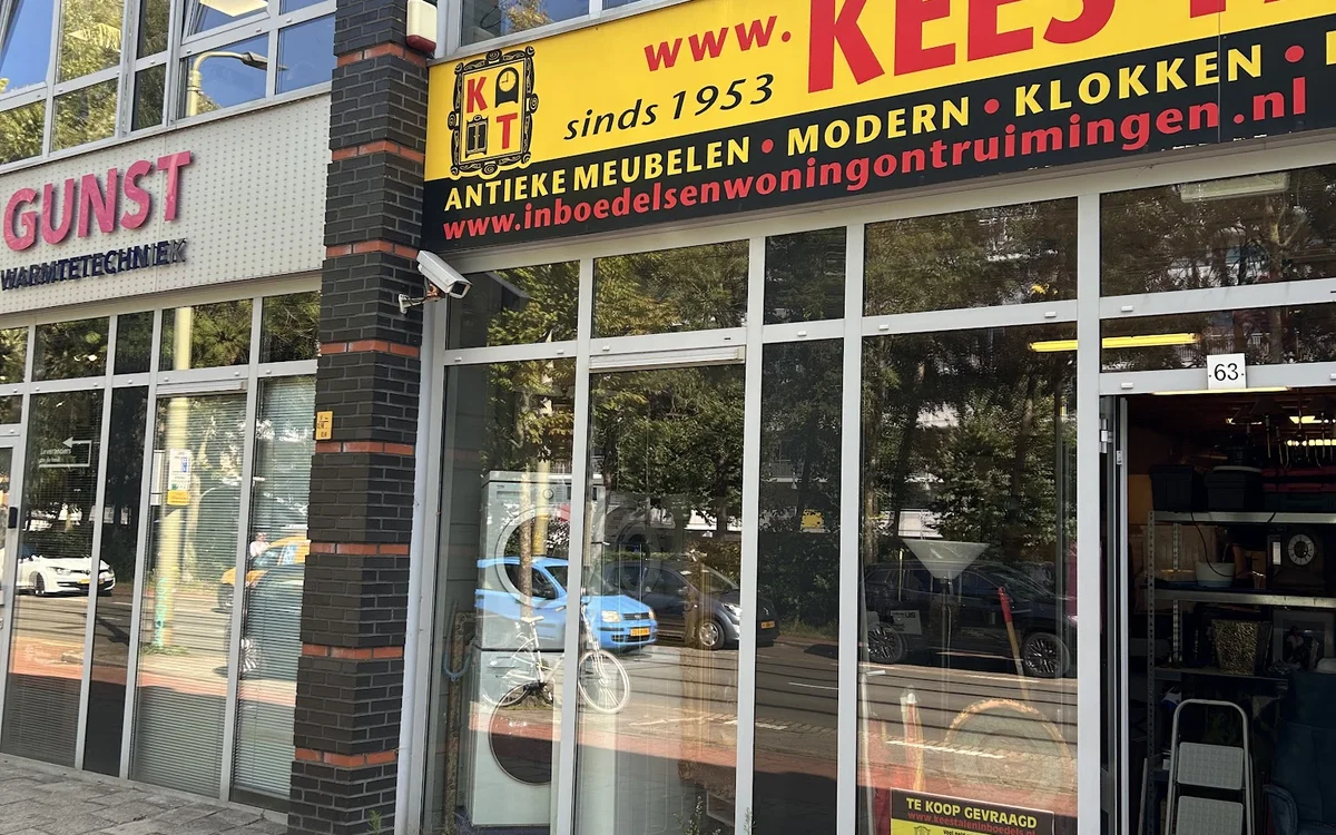 Winkelgevel met gele grijze letters en grote ramen, drukke straat met reflecties