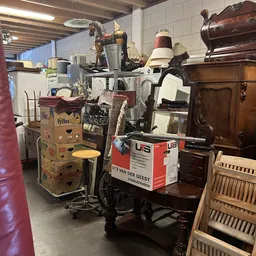 Diverse tweedehands huishoudelijke artikelen en meubels in de kringloopwinkel, waaronder een vintage friteuse en houten kaste