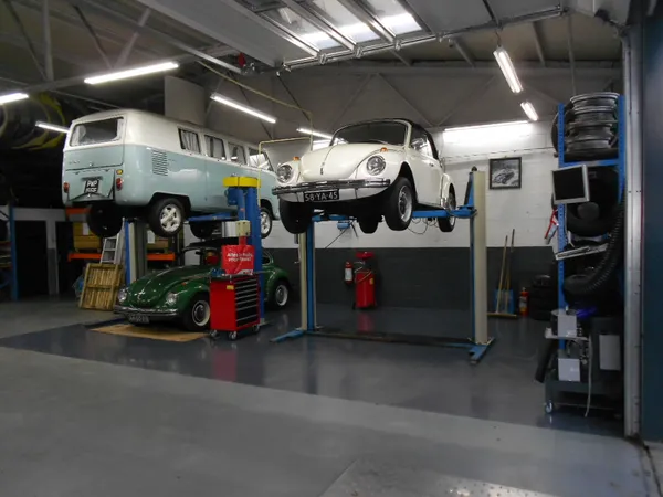 Werkplaats met twee klassieke Volkswagen Kever-auto's op hefbruggen, gereedschappen en onderdelen zichtbaar