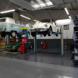 Werkplaats met twee klassieke Volkswagen Kever-auto's op hefbruggen, gereedschappen en onderdelen zichtbaar