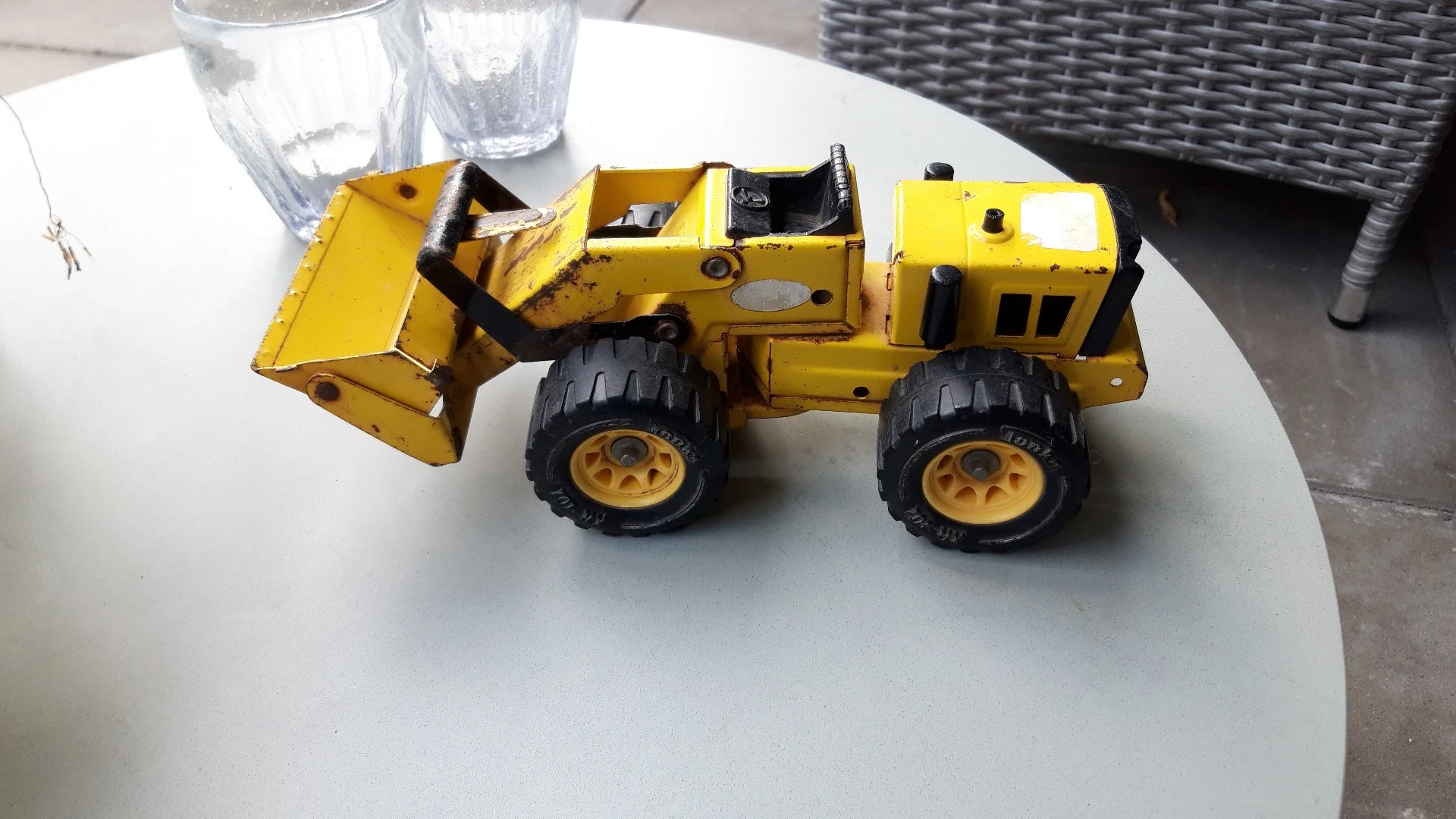 Gele speelgoedgraafmachine met zwarte wielen op een witte tafel