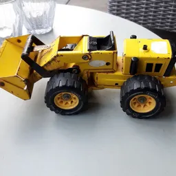 Gele speelgoedgraafmachine met zwarte wielen op een witte tafel