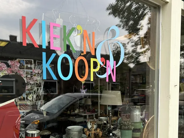 Gekleurde letters met winkelnaam op winkelruit, daarachter zichtbaar interieur met spullen
