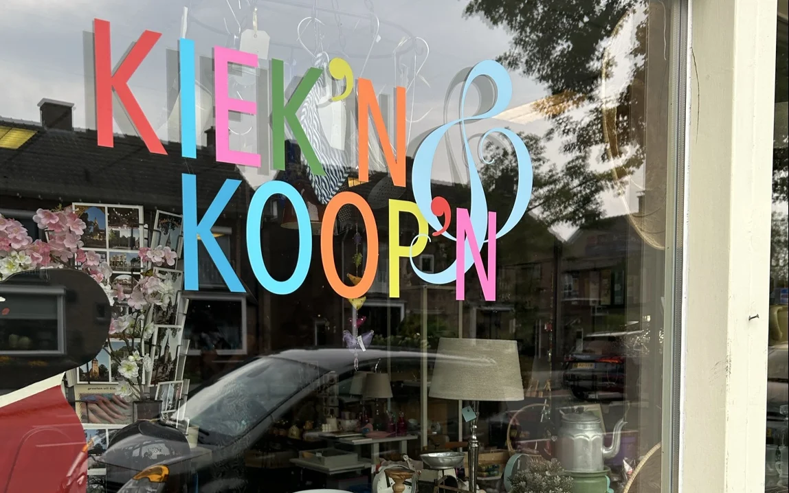 Gekleurde letters met winkelnaam op winkelruit, daarachter zichtbaar interieur met spullen