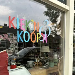 Gekleurde letters met winkelnaam op winkelruit, daarachter zichtbaar interieur met spullen