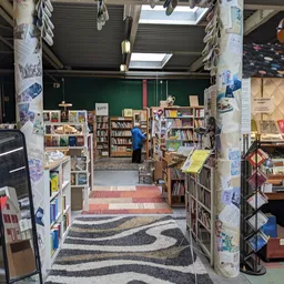 Binnenaanzicht van een kringloopwinkel met boekenkasten, stellingen en displays langs de zijkanten en een persoon die rondloo
