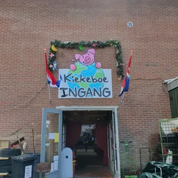 Bakstenen gevel met ingang en beschilderd welkomstbord met varken en Nederlandse vlag