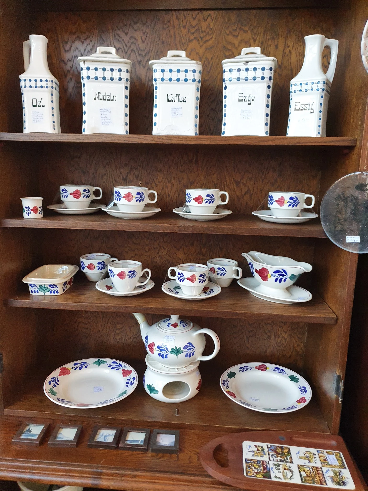 Houten kast met serviesgoed: kopjes, schotels en een theepot met blauwe en rode bloemenpatronen