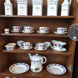 Houten kast met serviesgoed: kopjes, schotels en een theepot met blauwe en rode bloemenpatronen