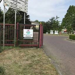Rode poort met bord Kringloopwinkel Kiekeboe en parkeerplaats op achtergrond
