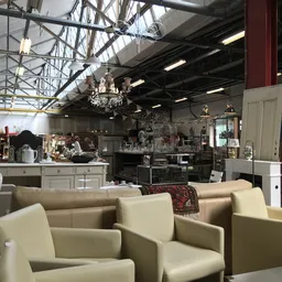Interieur van kringloopwinkel met beige fauteuils op de voorgrond, keukenmeubels en kroonluchter in de achtergrond