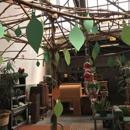 Interieur van kringloopwinkel met houten balkenstructuur, groene bladeren als decoratie, hangende rode ballen en diverse meub