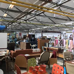 Winkelvloer met meubelen, kleding op rekken en diverse spullen onder industrieel plafond