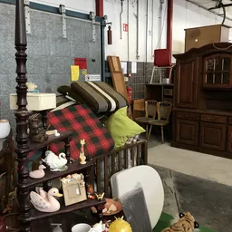 Tweedehands meubels en huishoudartikelen uitgestald in een kringloopwinkel, waaronder bedden, kasten en stoelen.