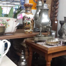 Uitgestalde antieke en vintage items: zilveren kannen, porseleinen vazen met bloemen, houten meubels en decoratieve objecten.